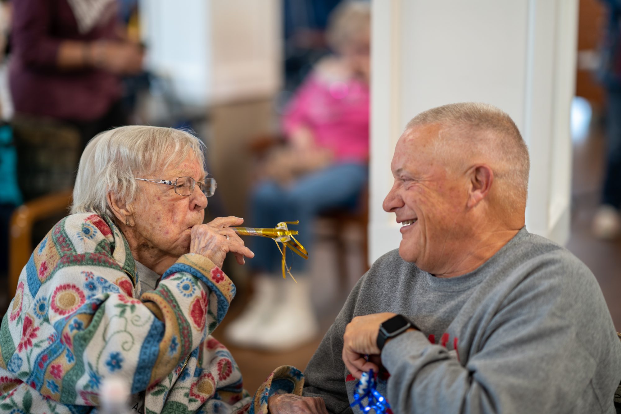 A woman blowing a party horn at a man while he laughs